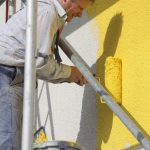 man painting exterior wall yellow on heights