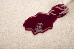 Red wine spilling from a glass onto a light coloured carpet.